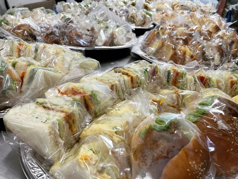 大皿に並べた個包装のパンとサンドイッチ