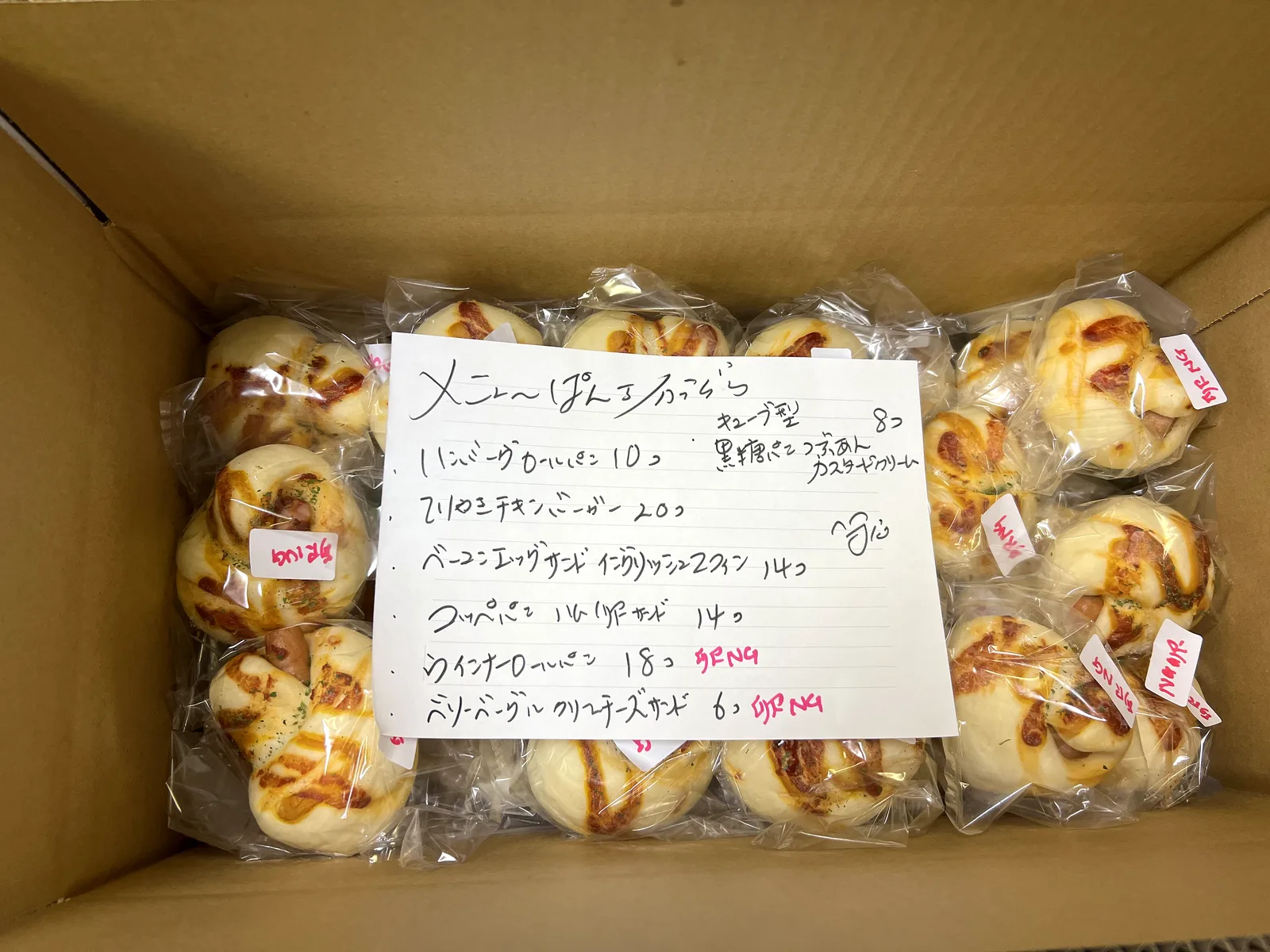 段ボールに詰めた個包装のパンと手書きのメニュー